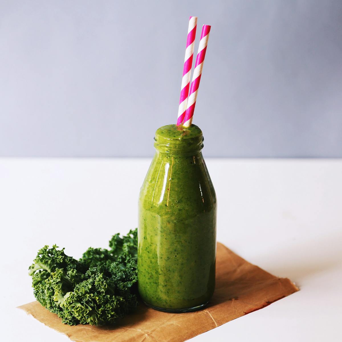 Energizing green smoothie with kale, served in a bottle with vibrant straws for a healthy lifestyle.