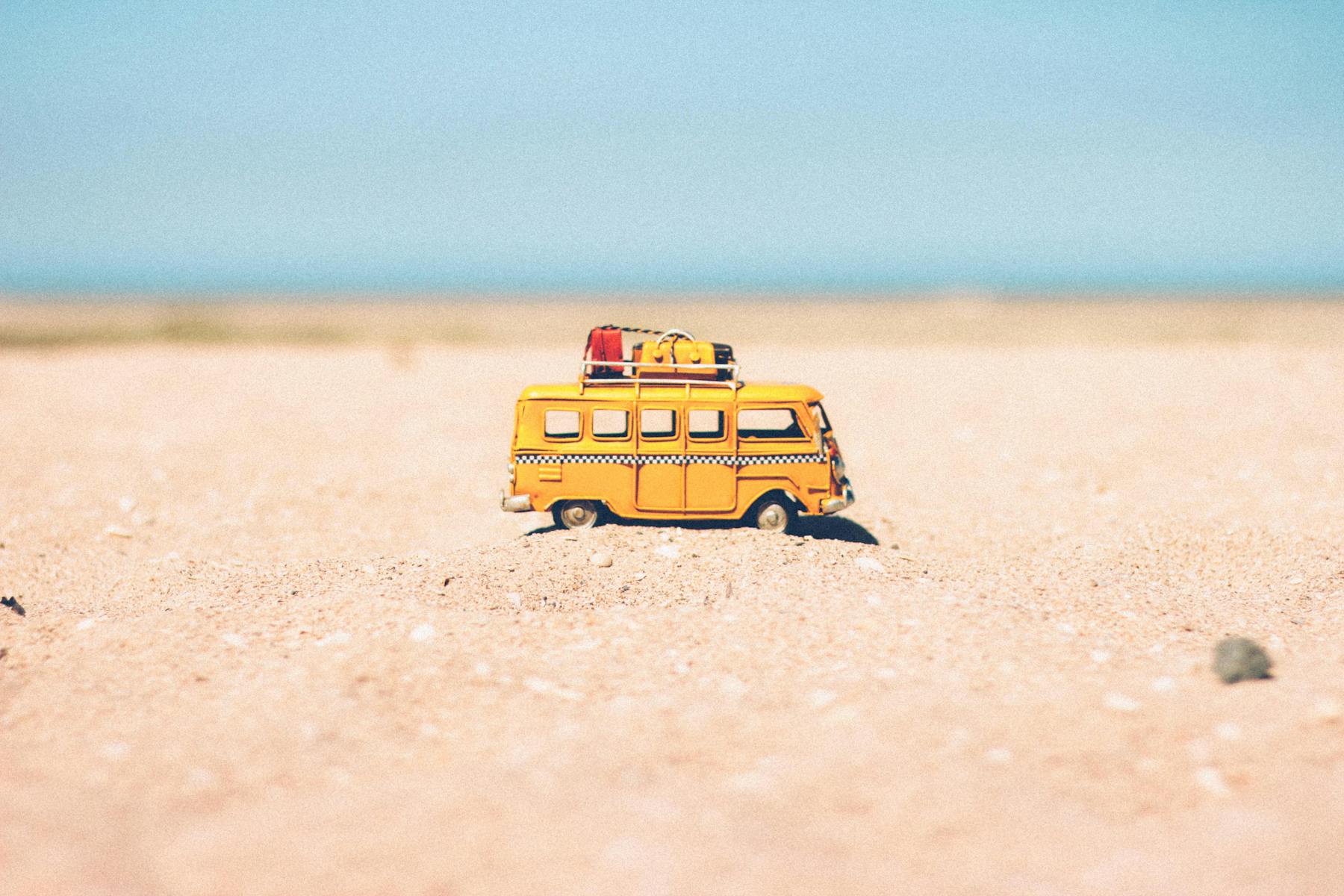 A toy van on a sandy beach evokes summer travel and vacation vibes.