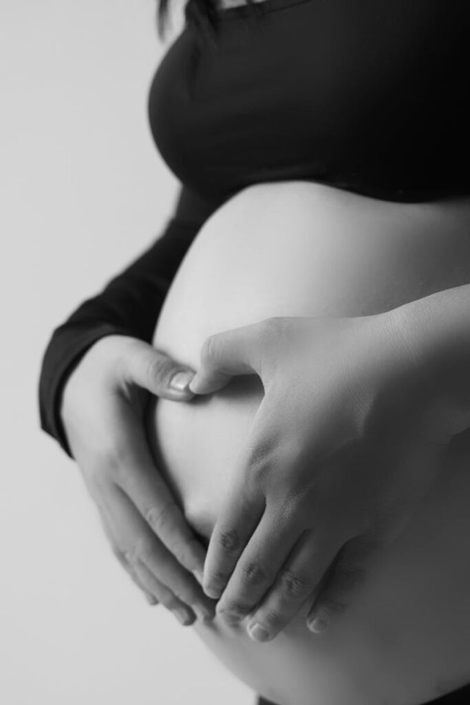 Monochrome image of a pregnant woman making a heart shape on her belly.