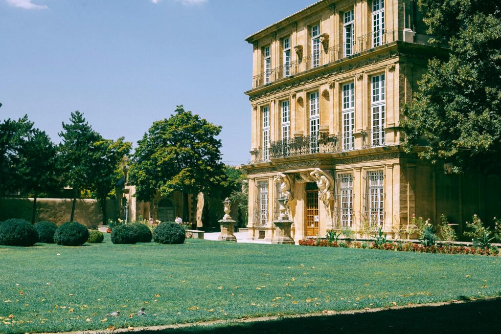 Facade of aged stone building decorated with sculptures and located near green trees and bushes