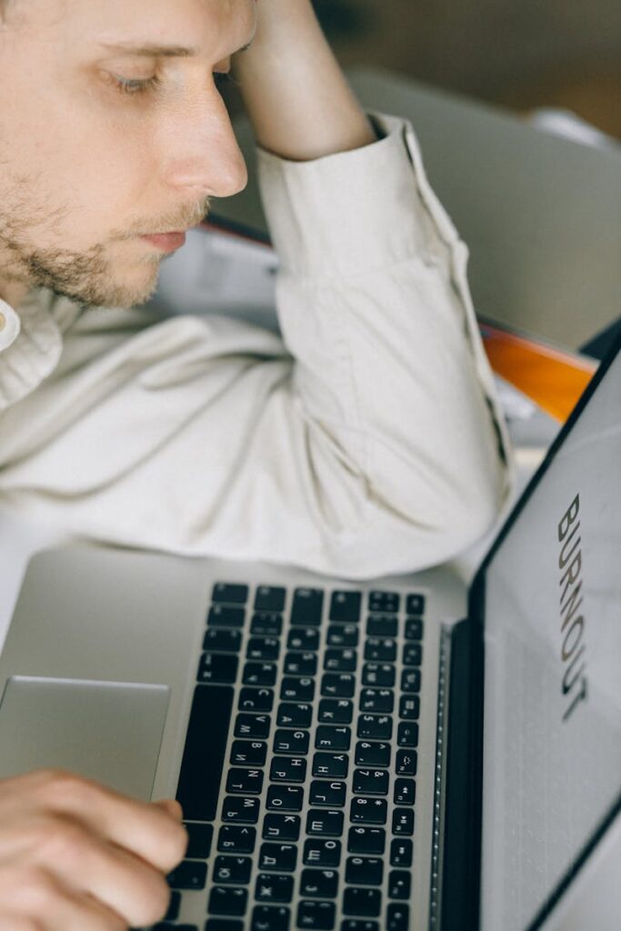 Tired employee leaning on laptop displaying 'Burnout', illustrating workplace stress.