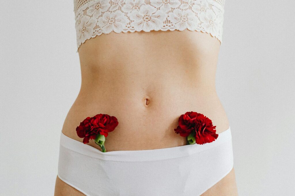 Close-up of a woman wearing white lingerie with red carnations. Delicate and artistic composition.
